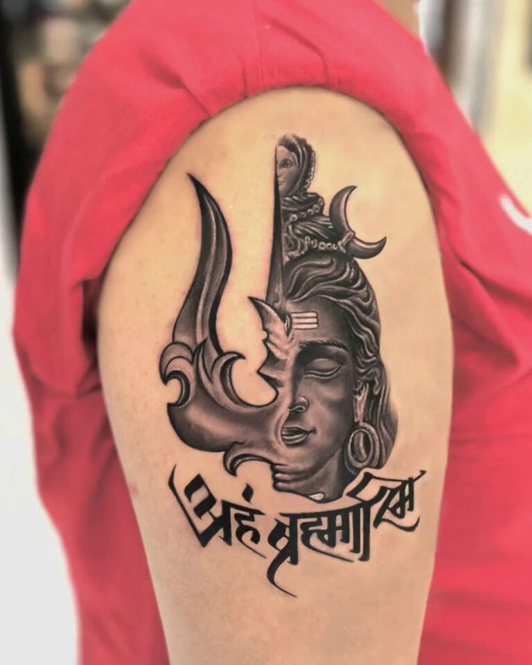 Black and grey Shiva Trishul tattoo on the upper arm with a Shiva portrait, crescent moon and Devanagari lettering